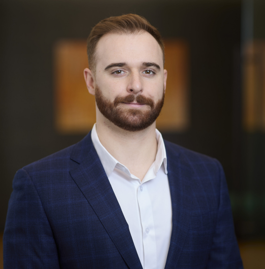 William Nemeth, a man with light skin, short brown hair, and a trimmed beard, wears a blue checked suit jacket and white shirt while posing against a blurred indoor background.