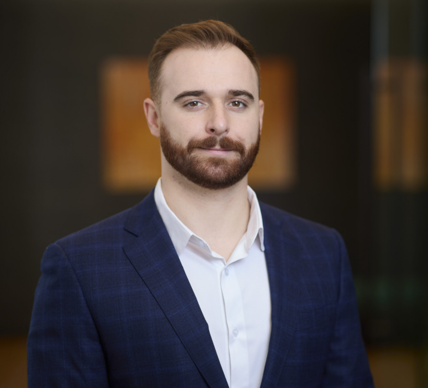 William Nemeth, a man with light skin, short brown hair, and a trimmed beard, wears a blue checked suit jacket and white shirt while posing against a blurred indoor background.