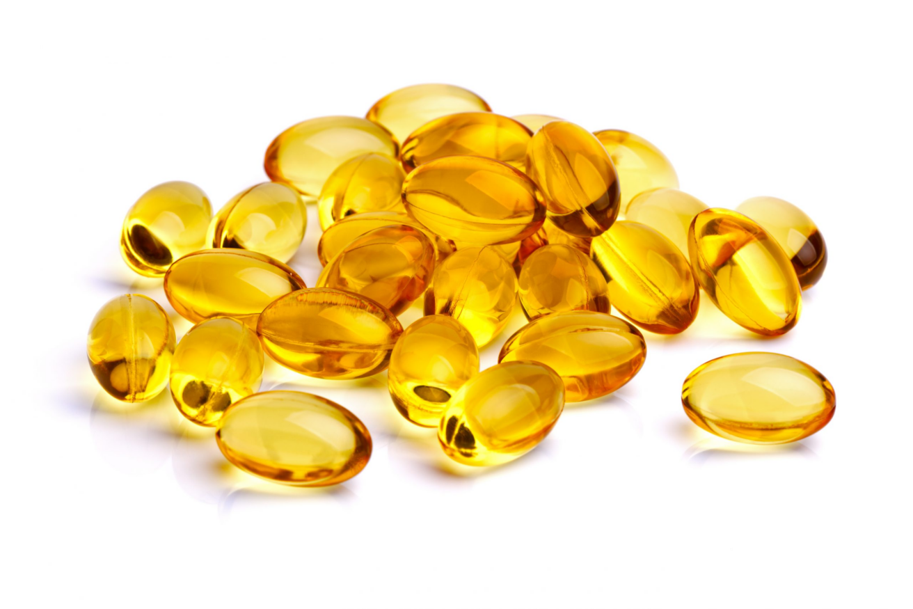 A pile of yellow, oval-shaped softgel capsules from Icelandirect is arranged on a white background. The capsules appear shiny and translucent, allowing light to pass through them.