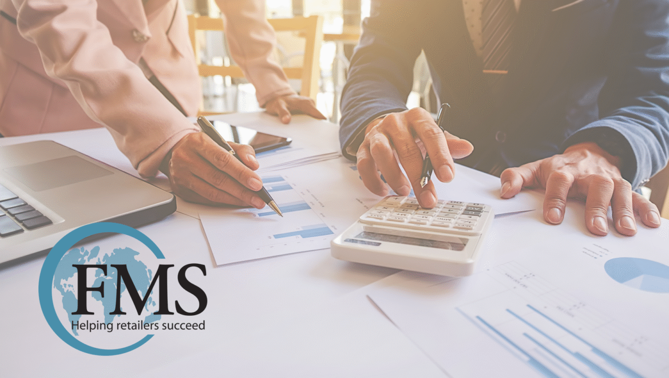 Two people in business attire review retail accounting charts and use a calculator at a desk. A laptop and documents are visible. The FMS logo with “Helping retailers succeed” appears in the bottom left corner.