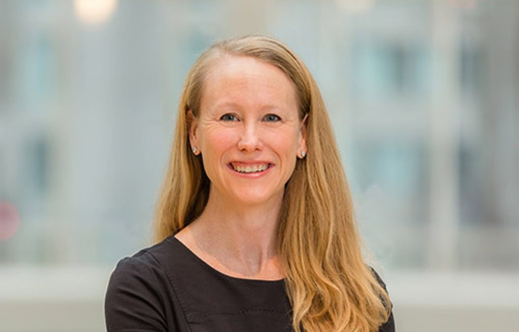 A woman with long blonde hair, wearing a black top, smiling while standing indoors in front of a blurred background, embodies the spirit of operations best practices featured in PFM Magazine.