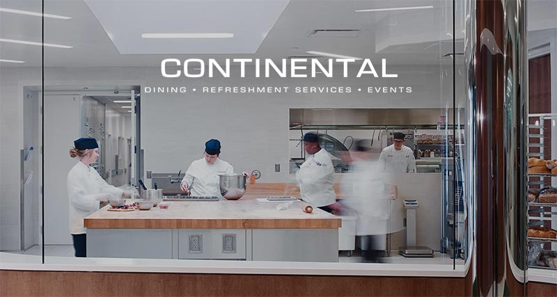 Four chefs in white uniforms and dark hats work in a modern, clean kitchen behind glass. Above them, "CONTINENTAL SERVICES • REFRESHMENT SERVICES • EVENTS" is displayed, highlighting the venue's investment in culinary heritage and excellence.