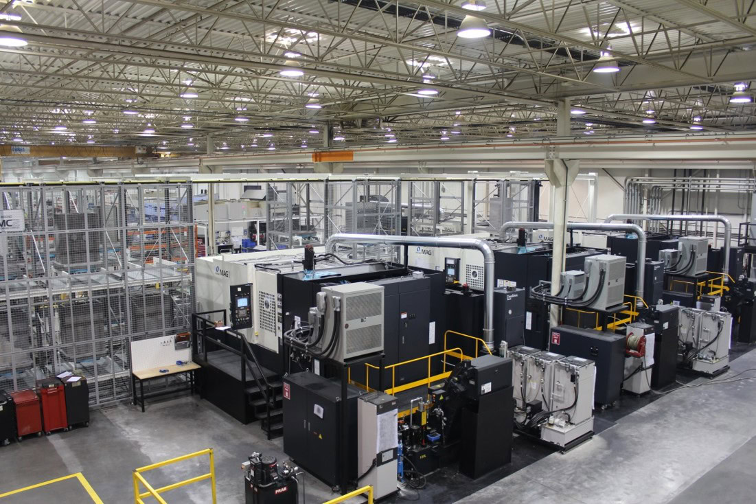 A large, brightly lit industrial facility at Centra Industries features several black and gray CNC machines lined up, surrounded by safety railings and metal structures, under a high ceiling with lights and exposed beams. Heritage Exits are clearly marked throughout.