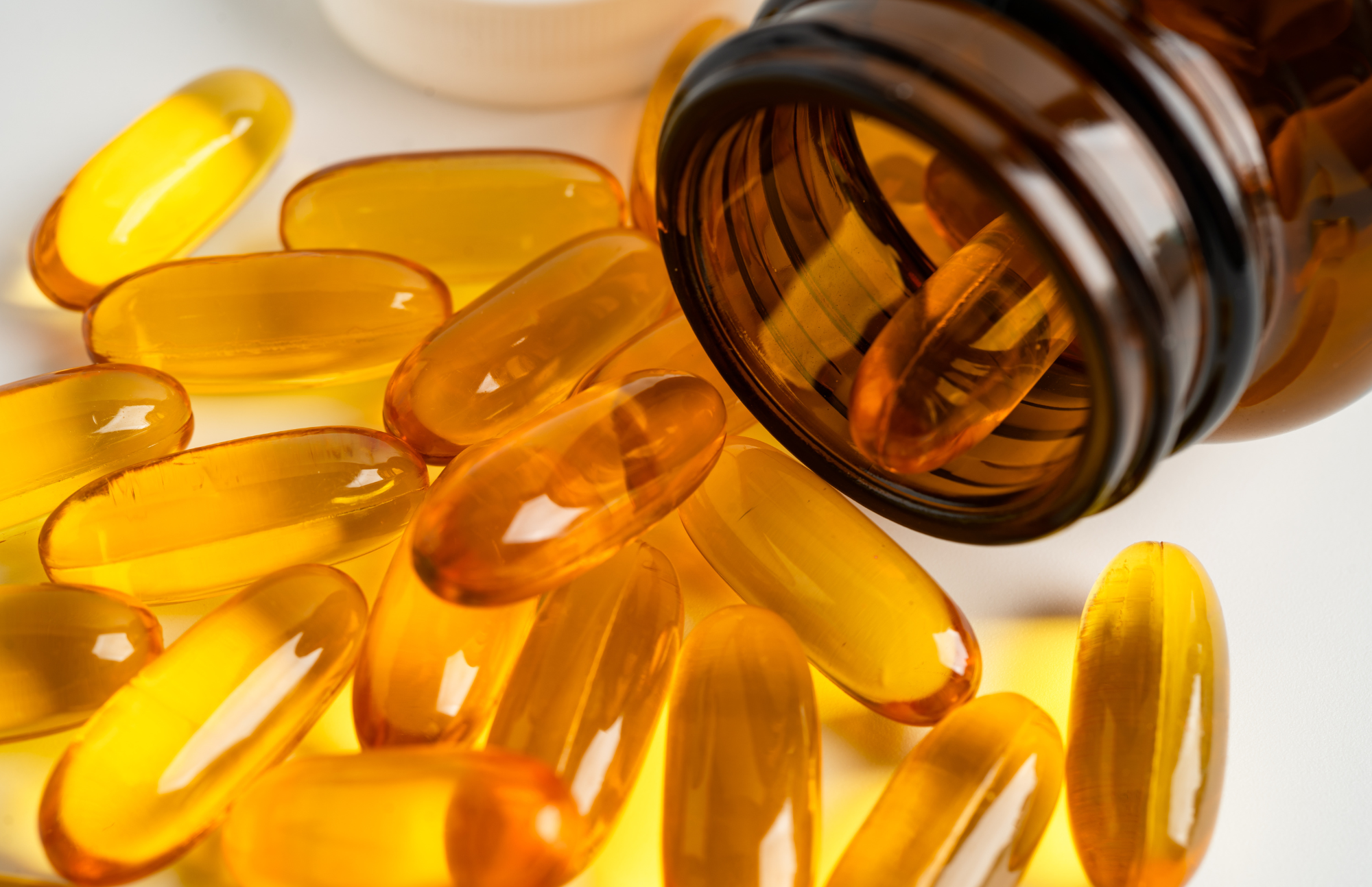 A brown glass bottle from Icelandirect is tipped on its side, with several yellow translucent gel capsules spilling out onto a white surface.