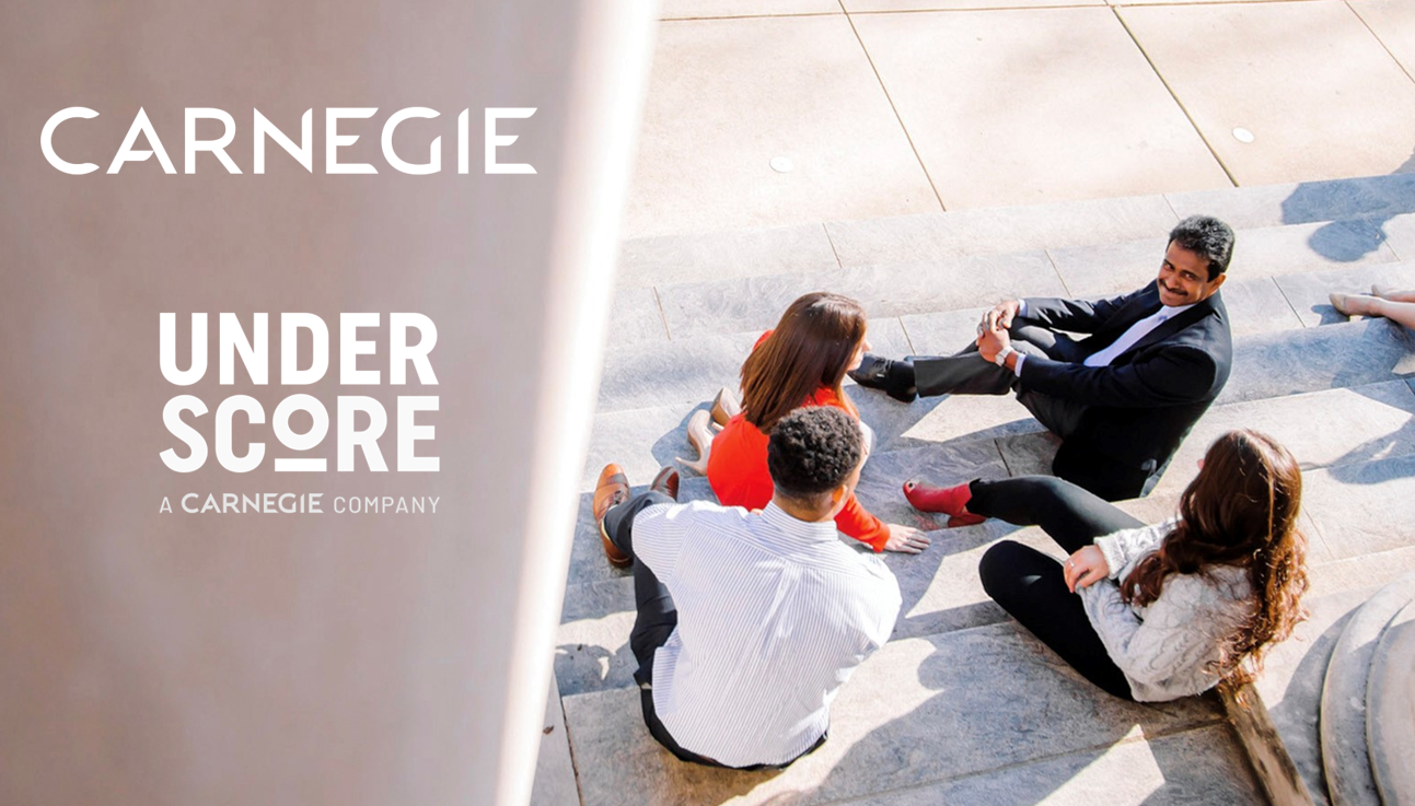 Five people sit in a circle on outdoor steps, engaged in a discussion. Sunlight casts shadows across the stone steps. The words “CARNEGIE” and “UNDERSCORE: A Carnegie Company” highlight their connection after the merger.