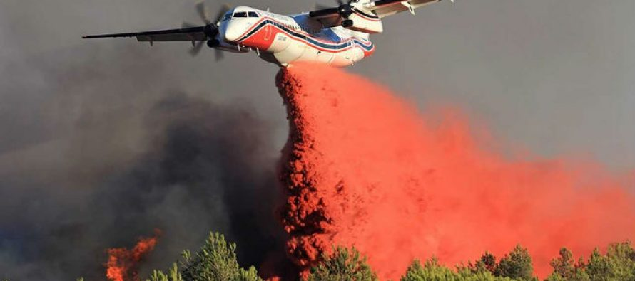 A Conair Q400MR firefighting airplane releases a large cloud of red fire retardant over a forest fire, with dark smoke and flames rising from the trees below, showcasing its special mission interiors in action.