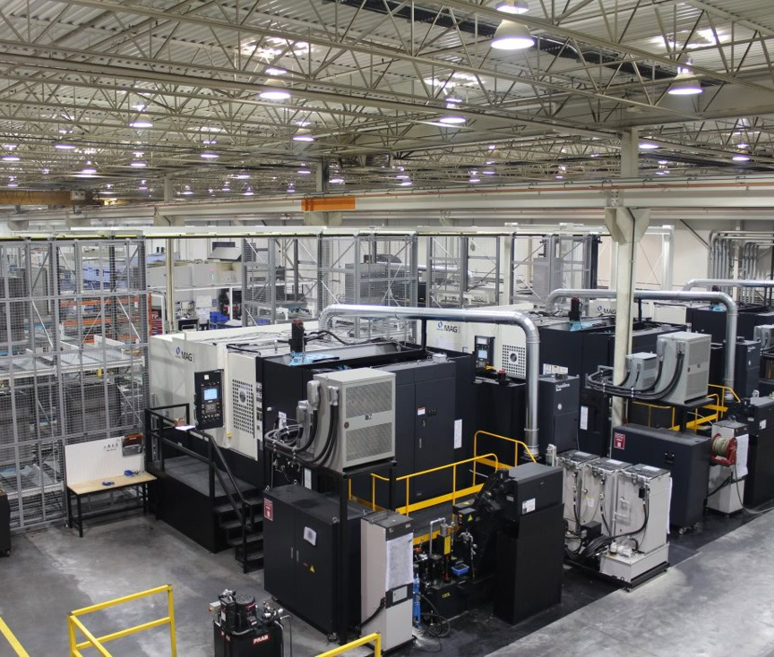 A large, brightly lit industrial facility at Centra Industries features several black and gray CNC machines lined up, surrounded by safety railings and metal structures, under a high ceiling with lights and exposed beams. Heritage Exits are clearly marked throughout.