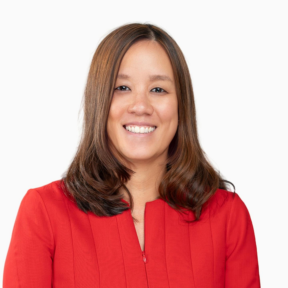 A woman with straight, shoulder-length brown hair is smiling. She is wearing a bright red top and is posed against a plain white background.