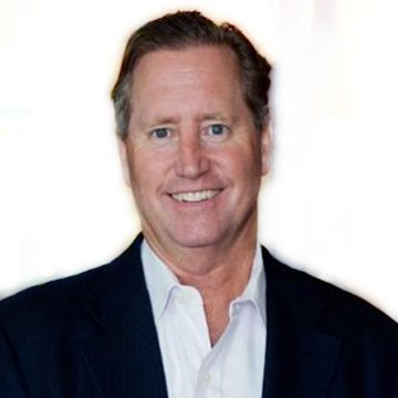A middle-aged man with short brown hair is wearing a dark suit jacket and a white shirt, smiling at the camera against a plain, light background.