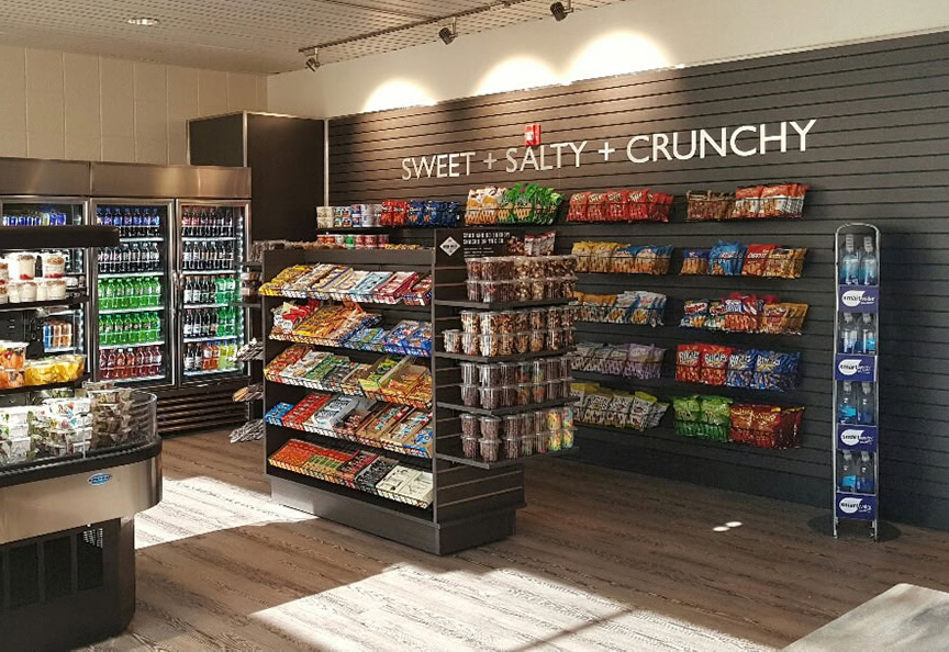 A convenience store with shelves filled with chips, snacks, and drinks. A sign on the wall reads "SWEET + SALTY + CRUNCHY." Coolers with beverages line the left side—an ideal Case Study for Continental Services' innovative food and drink solutions.