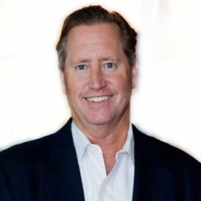 A middle-aged man with short brown hair is wearing a dark suit jacket and a white shirt, smiling at the camera against a plain, light background.