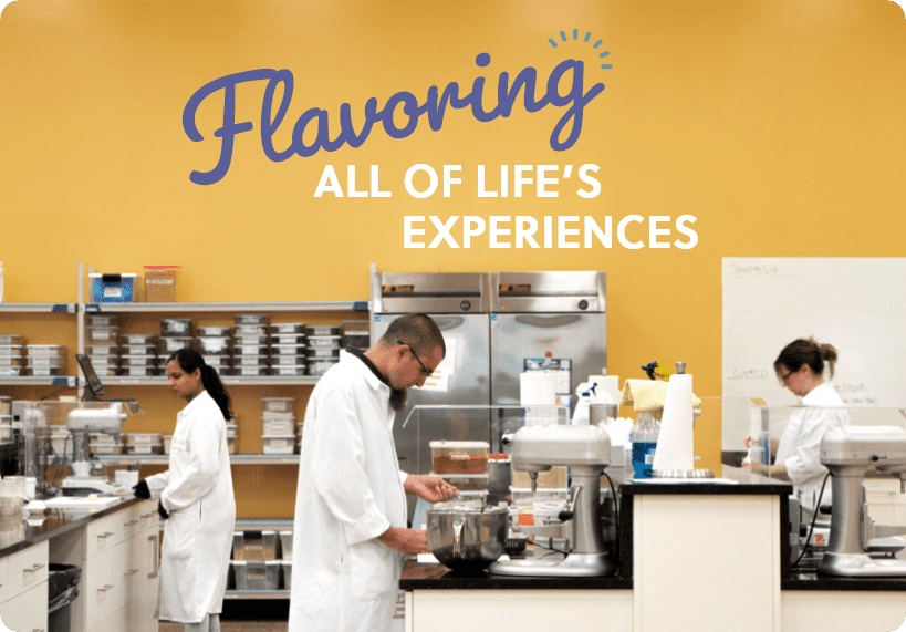 Three people in white lab coats work in a bright, organized laboratory kitchen at Revela Foods, with mixers and shelves. On the yellow wall above them is the text, “Flavoring All of Life’s Experiences.” Perfect for an SEO case study visual.
