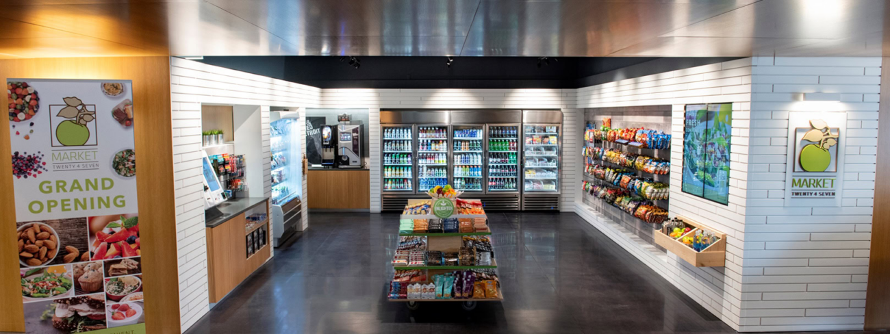 A modern Continental Services convenience store interior with refrigerated drinks, snacks on shelves, a coffee station, and “Grand Opening” signs on white walls. The store is brightly lit and neatly organized.