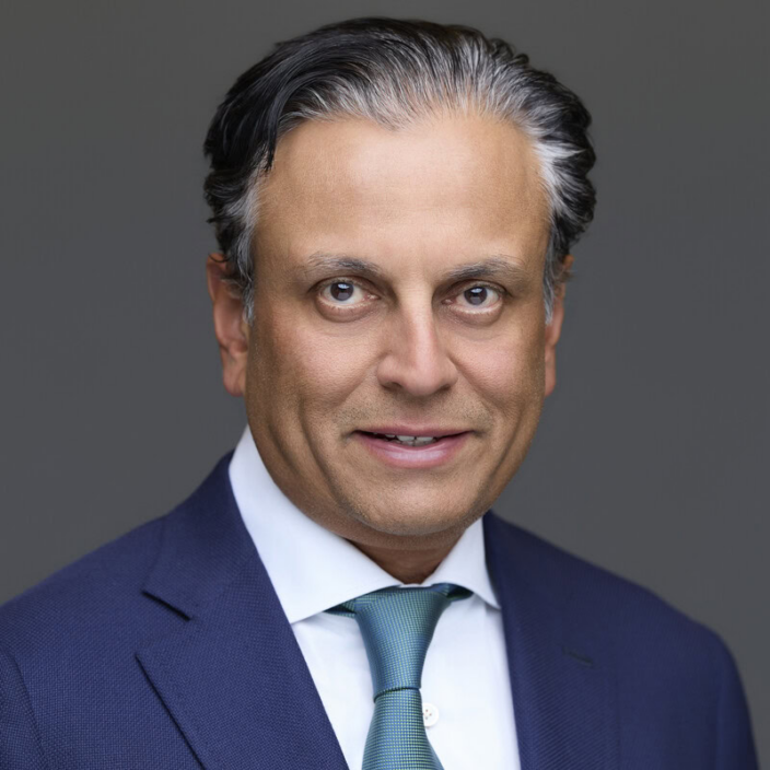 A middle-aged man with dark, slicked-back hair and light skin, dressed in a blue suit, white shirt, and teal tie, smiles slightly while posing against a neutral gray background—perfect for a Regions Securities executive profile.