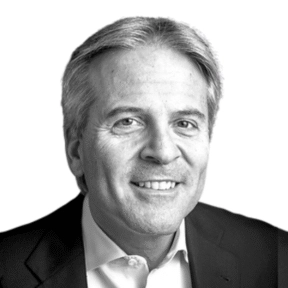 A middle-aged man with gray hair, wearing a white dress shirt and a dark blazer, smiling at the camera against a white background.