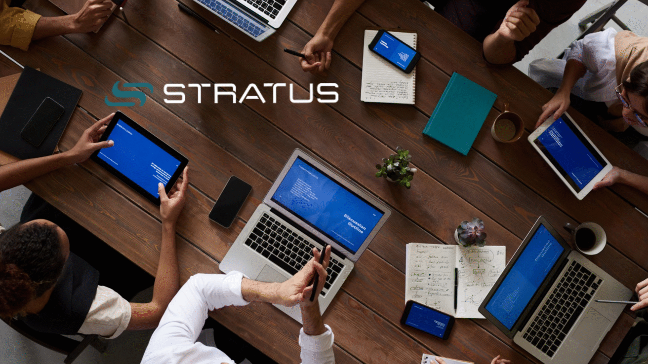 A group of people sit around a wooden table with laptops, tablets, phones, notebooks, and coffee, working together. The word "STRATUS" and a logo appear over the image, reflecting the collaborative spirit behind an Investment Exit.