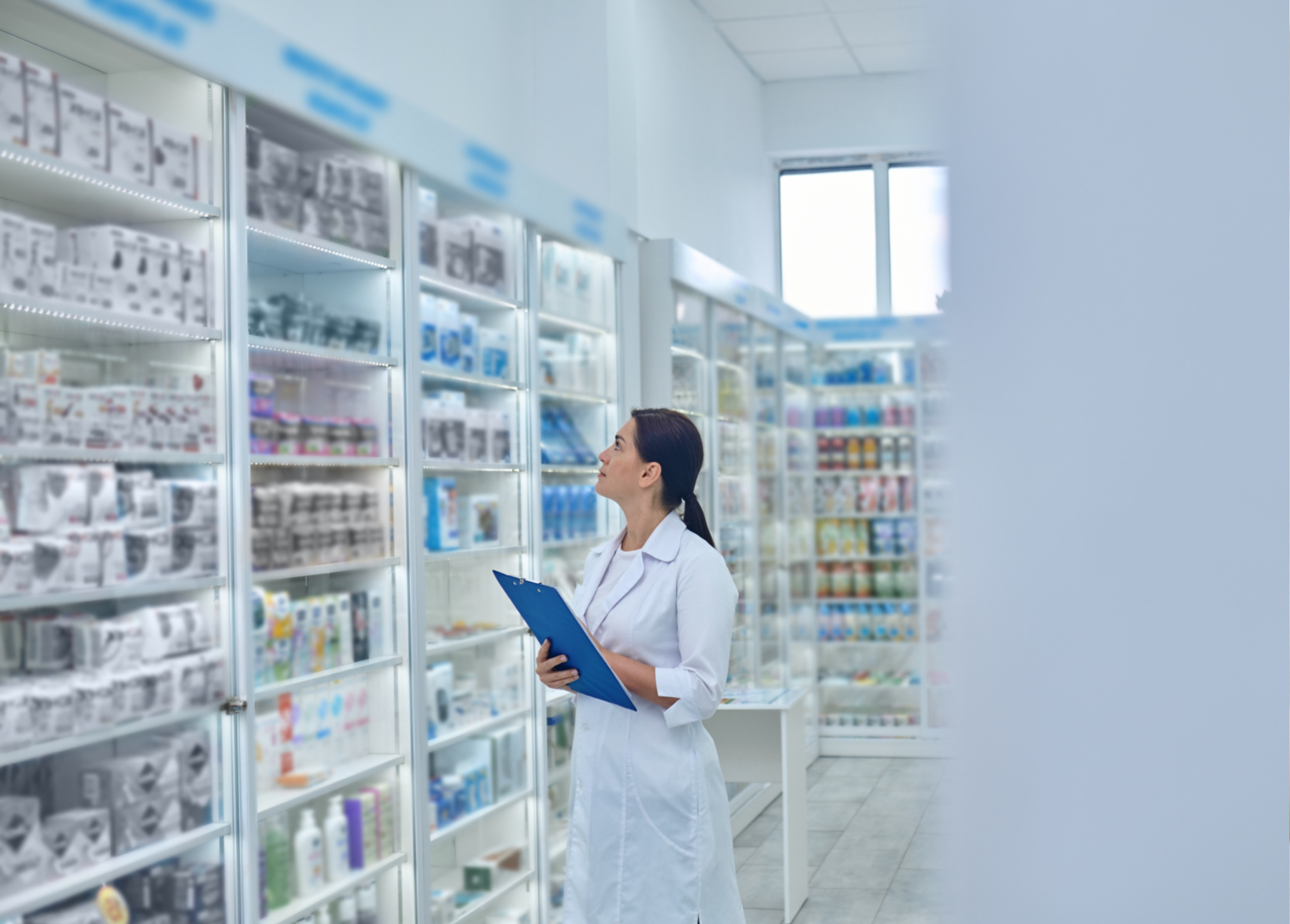 A pharmacist in a white coat holds a blue clipboard while examining shelves filled with various medical products and brilliant gifts in a brightly lit pharmacy.
